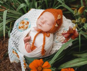 newborn baby wearing orange hat sleeping in bucket in flowers near Charlotte nc