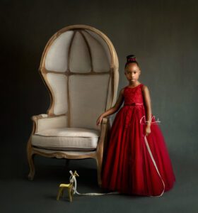 child wearing red dress standing by large chair