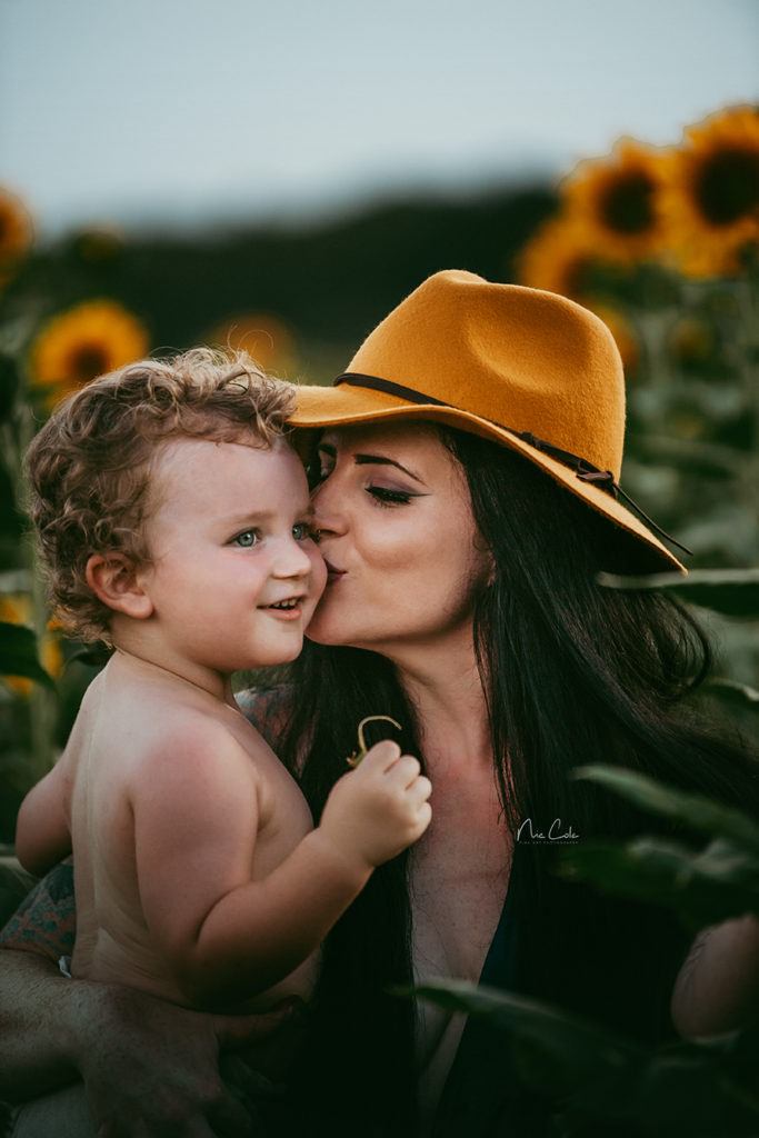 mother kissing her baby boy in sunflower fields