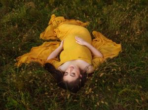 expecting mother laying on ground in yellow maternity gown