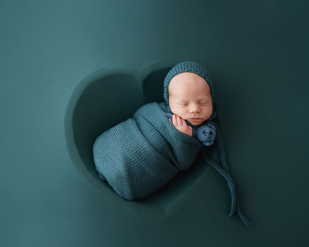 baby sleeping in blue wooden heart bowl