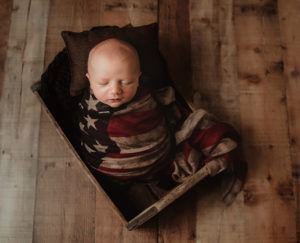 A baby image of newborn sleeping in crate with American Flag